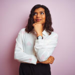 Transsexual transgender businesswoman standing over isolated pink background with hand on chin thinking about question, pensive expression. Smiling with thoughtful face. Doubt concept.