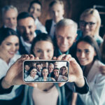 Close up blurry photo business people different age race free time excited team building hug embrace cuddle she her he him his telephone smart phone make take selfies formal wear jackets shirts